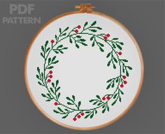 a cross stitch christmas wreath with red berries and green leaves is shown in the hoop