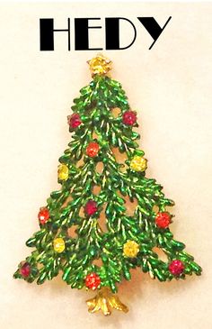 "Christmas tree pin signed, \"Hedy\" is pictured on Page 35 of May Morrison's, \"Christmas Jewelry.\" It is also pictured on Page 71 of Nancy Trowbridge's, \"O Christmas Tree\".  This color palette is so much the Mod colors of its time.  It features ruby red, orange/red, and yellow rhinestone ornaments on a green metallic tree in gold tone metal. This color combination in this tree is very hard to find, This wonderful Hedy signed Christmas tree pin measures approximately 2-1/4 x 1-3/4\" and has Christmas Brooches, Rhinestone Ornaments, O Christmas Tree, Tree Jewelry, Jewelry Christmas Tree, Book Pieces, Holiday Pins, Red Orange Yellow, Christmas Pins