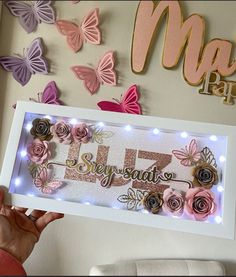 a woman holding up a framed photo with flowers and butterflies on the wall behind her