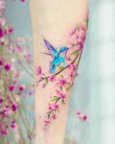 a small blue bird sitting on top of a tree branch with pink flowers around it