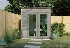 a small garden shed sitting in the middle of a yard with grass and bushes around it