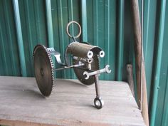 a metal object with gears attached to it on a wooden platform in front of a green wall