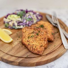 two pieces of chicken on a cutting board with coleslaw and lemon wedges