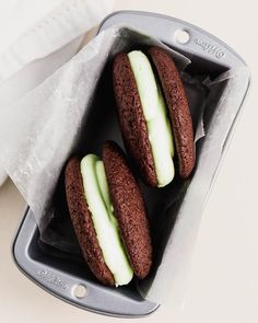 three chocolate cookies with green frosting in a baking pan on a counter top next to a napkin