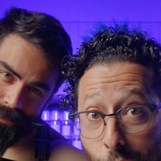 two men with glasses and beards are posing for a photo in front of a purple background