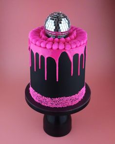 a cake with pink icing and a disco ball on top is sitting on a black stand