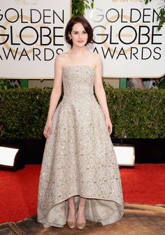 a woman in a strapless dress standing on a red carpet with her hands behind her back