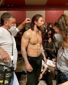 a man with long hair and no shirt standing in front of other people wearing face masks