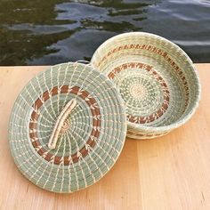 two woven baskets sitting on top of a wooden table next to water and boats in the background