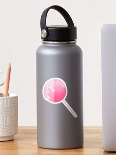 a pink lollypop sticker on a gray water bottle next to a white laptop