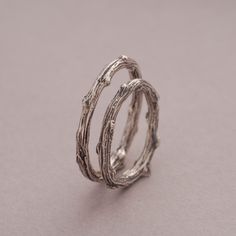 two silver rings made out of branches sitting on top of a gray surface with one ring in the middle