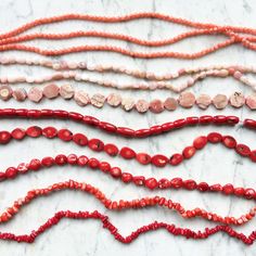 red and white beaded necklaces laid out on a marble counter top, including coral beads