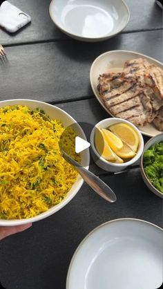 a person is holding a bowl of food with lemons and other foods on the table