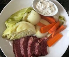 a white plate topped with meat, carrots and celery next to a bowl of dip