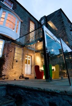 a modern house with glass walls and colorful chairs in the front yard at night time