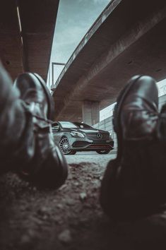 two men's shoes sitting on the ground next to a car under a bridge