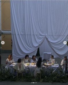 a group of people sitting around a table with food on it and white drapes over them