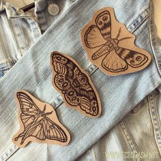 three wooden butterfly magnets sitting on top of a pair of jeans