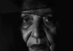 an old woman with her hands on her face looking at the camera in black and white