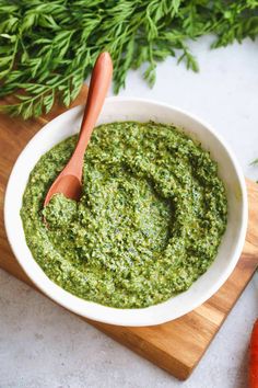 a white bowl filled with pesto on top of a wooden cutting board next to carrots