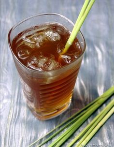 a glass with ice and some green onions on the side, next to two stalks of grass