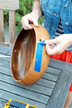 a person is holding a wooden bowl with a blue tape on the bottom and an orange piece of wood in front of them