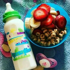 a blue bowl filled with fruit next to a baby's sippy bottle and cereal