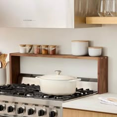 a stove top oven sitting inside of a kitchen next to a wooden shelf filled with glasses