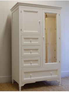 a white armoire sitting on top of a hard wood floor next to a wall