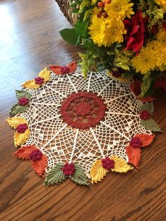 a crocheted doily with flowers in the center on a wooden table next to a wicker basket