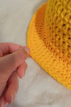 a hand is holding the edge of a yellow crocheted hat on a white furnishing