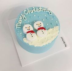 two snowmen sitting on top of a blue frosted cake