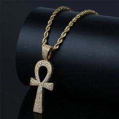 an egyptian cross pendant with white diamonds on a gold chain, sitting on top of a black