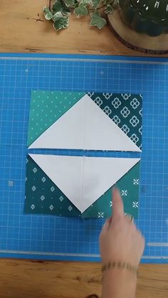 someone is making an origami envelope out of paper on a cutting board next to a potted plant