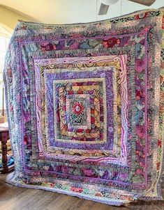 a large quilt hanging from the ceiling in a room with wooden floors and windows,