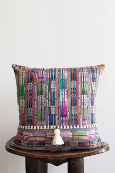 a colorful pillow sitting on top of a wooden table next to a white wall with a tassel hanging from it