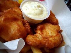 some fried food is sitting on a white paper with a lemon wedge and sauce in it