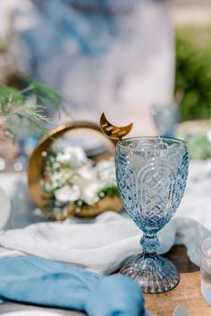 a blue glass with a gold bird on it sitting on top of a wooden table