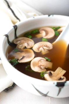 a white bowl filled with soup and mushrooms on top of a table next to napkins