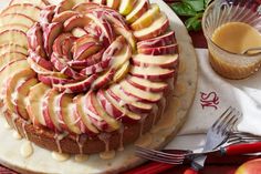 a cake with apples and icing on it sitting next to some utensils