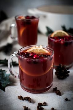 two mugs filled with cranberry tea and orange slices on top of a table