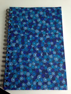 a spiral notebook with blue and black circles on the cover, next to a pen