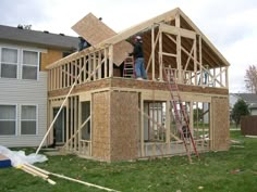 a man standing on top of a wooden structure in front of a house under construction