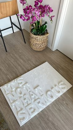 a white door mat with the words welcome home and purple flowers in a basket next to it