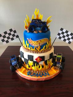 a birthday cake decorated with monster trucks and checkered flags on a wooden table in front of a white wall