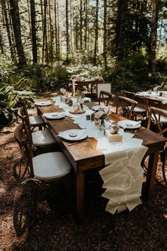 a table set up for an outdoor dinner in the woods with plates and napkins on it