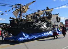 people are walking down the street in front of a large boat that is being paraded