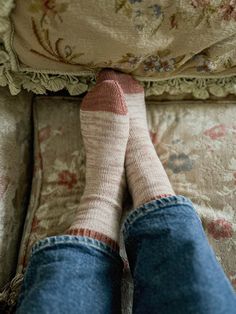 the feet of a person wearing socks and jeans on a bed with floral pillows,