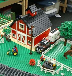 a toy farm with horses and tractors on the ground next to a red building that is made out of legos