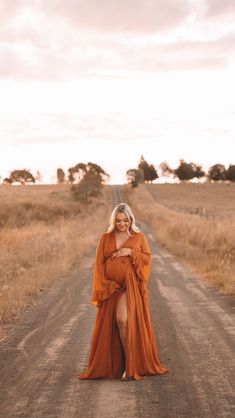 a woman in an orange dress is standing on a dirt road with her legs crossed